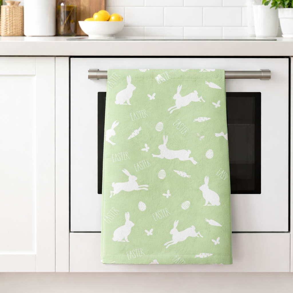Green towel with white bunny pattern hanging on a kitchen oven handle.