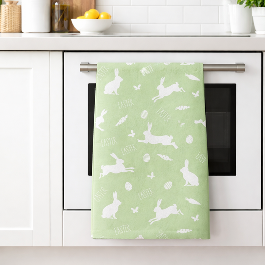 Green towel with white bunny pattern hanging on a kitchen oven handle.