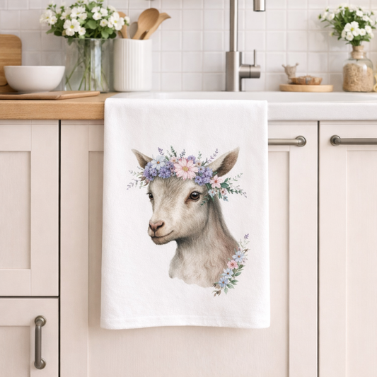 Kitchen towel with a goat illustration and floral crown hanging on a kitchen cabinet.